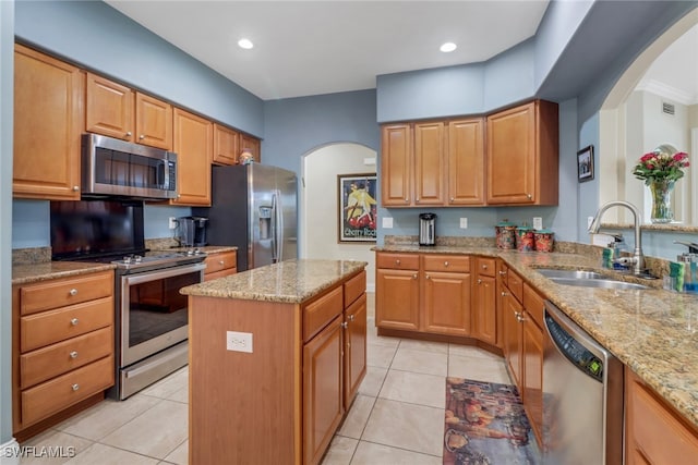 kitchen with appliances with stainless steel finishes, a center island, a sink, and light stone counters