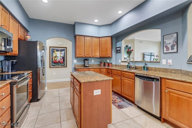 kitchen with appliances with stainless steel finishes, light stone counters, a center island, a sink, and light tile patterned flooring