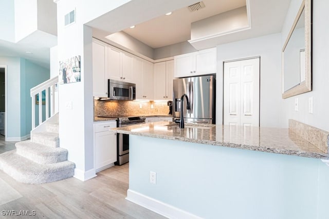 kitchen featuring kitchen peninsula, decorative backsplash, white cabinetry, light stone countertops, and stainless steel appliances