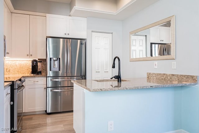 kitchen featuring kitchen peninsula, sink, white cabinetry, stainless steel appliances, and light stone counters