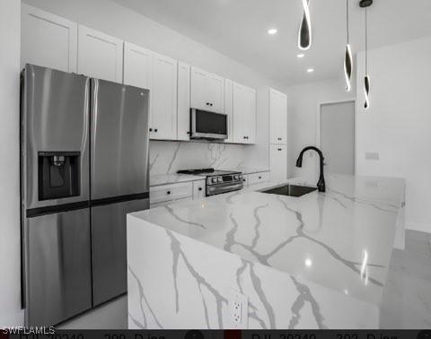 kitchen with white cabinets, stainless steel appliances, sink, and light stone countertops