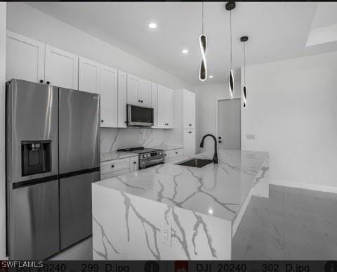 kitchen with an island with sink, appliances with stainless steel finishes, light stone countertops, and sink