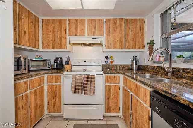 kitchen featuring sink, light tile patterned floors, dark stone counters, and appliances with stainless steel finishes