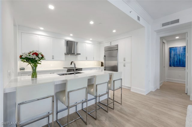 1030 3rd Ave S Unit 419, Naples, FL 34102 - kitchen featuring wall chimney range hood, stainless steel fridge, a breakfast bar, white cabinetry, and light countertops