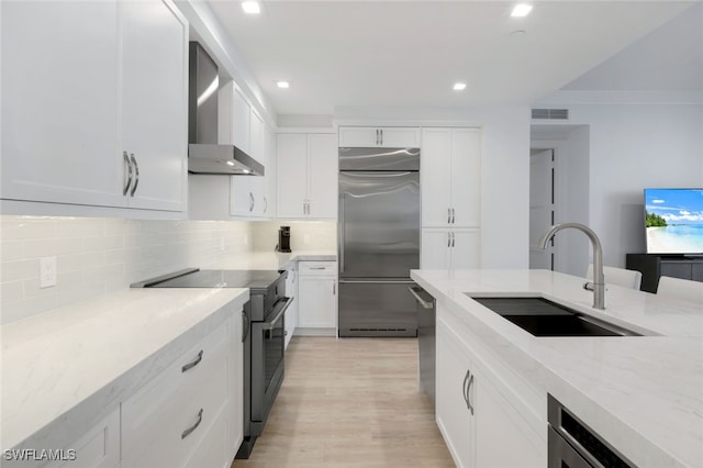 kitchen with white cabinetry, stainless steel appliances, light stone countertops, wall chimney exhaust hood, and sink