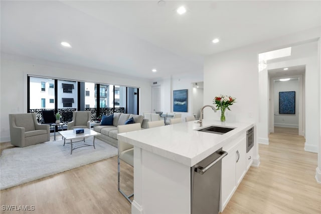 kitchen featuring white cabinetry, light hardwood / wood-style floors, a kitchen island with sink, dishwasher, and sink