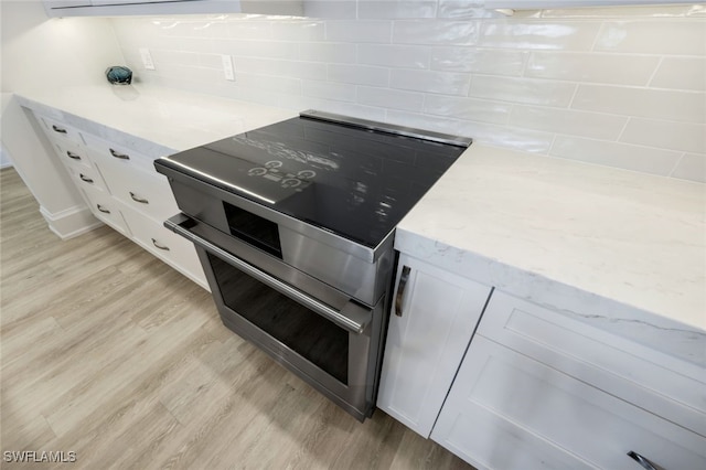 kitchen with electric stove, backsplash, white cabinets, and light wood-type flooring