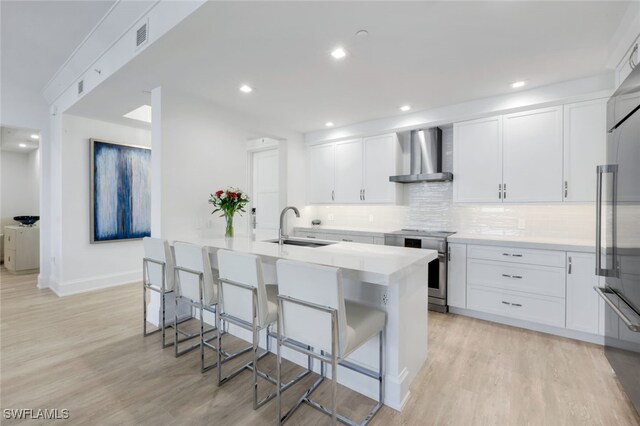 1030 3rd Ave S Unit 419, Naples, FL 34102 - kitchen featuring wall chimney exhaust hood, stainless steel appliances, a sink, a breakfast bar, and light wood-style floors
