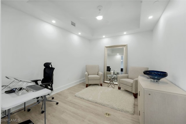 home office with light hardwood / wood-style floors and a raised ceiling