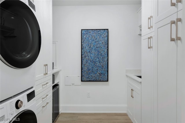 laundry room with cabinets, stacked washer and dryer, and light wood-type flooring