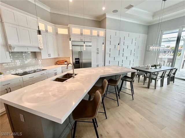 kitchen featuring stainless steel built in fridge, sink, white cabinetry, and an island with sink