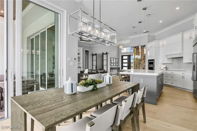 dining space with a notable chandelier, light wood-type flooring, a barn door, and ornamental molding