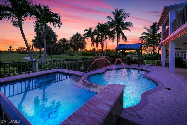 pool at dusk with a patio and pool water feature