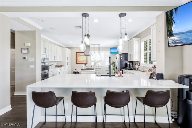 kitchen with white cabinets, a kitchen bar, kitchen peninsula, hanging light fixtures, and dark wood-type flooring