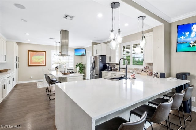 kitchen with island exhaust hood, kitchen peninsula, stainless steel fridge, sink, and decorative light fixtures