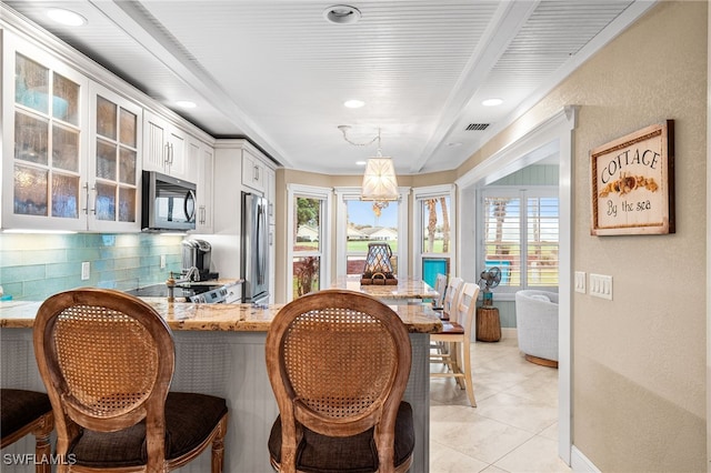 kitchen with white cabinetry, appliances with stainless steel finishes, decorative backsplash, pendant lighting, and light stone counters