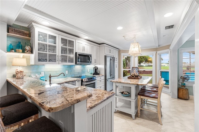 kitchen with decorative light fixtures, stainless steel appliances, tasteful backsplash, kitchen peninsula, and a breakfast bar