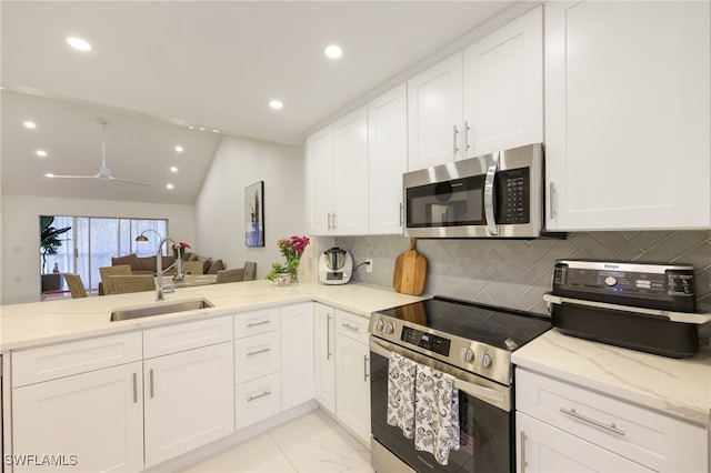 kitchen with stainless steel appliances, kitchen peninsula, sink, white cabinetry, and lofted ceiling