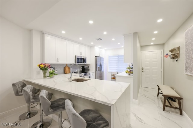 kitchen with white cabinetry, kitchen peninsula, backsplash, a breakfast bar, and appliances with stainless steel finishes