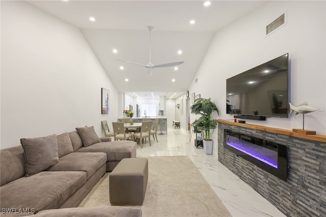 living room with high vaulted ceiling, ceiling fan, and a stone fireplace