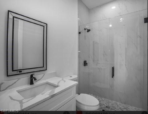 bathroom featuring a shower with door, vanity, and toilet