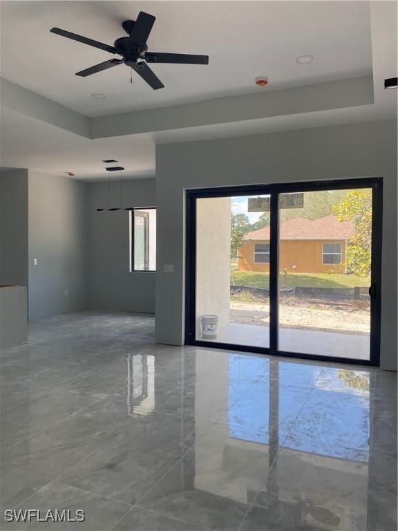 empty room featuring a tray ceiling, marble finish floor, and a healthy amount of sunlight