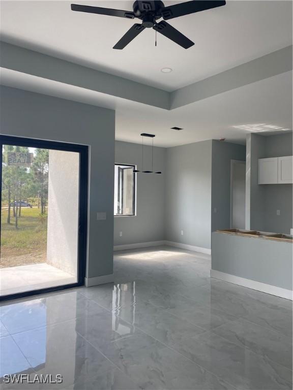 empty room with a ceiling fan, a tray ceiling, and baseboards