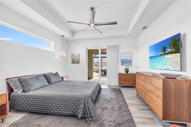 bedroom featuring access to outside, light hardwood / wood-style floors, a raised ceiling, and ceiling fan