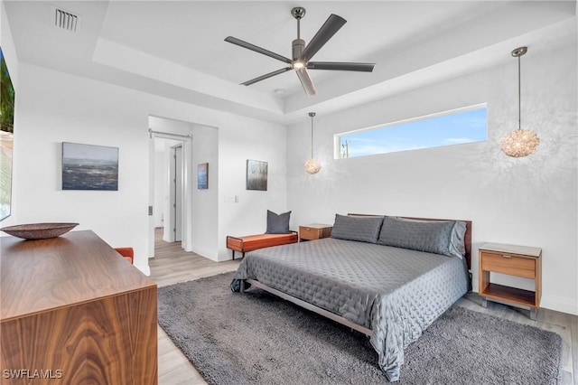 bedroom featuring light hardwood / wood-style flooring, a raised ceiling, and ceiling fan