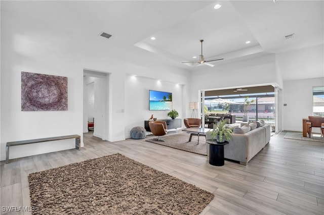 living room featuring ceiling fan, a tray ceiling, and light hardwood / wood-style floors