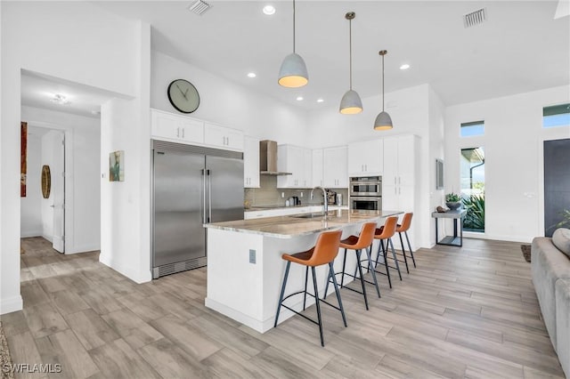 kitchen featuring appliances with stainless steel finishes, pendant lighting, white cabinets, light stone countertops, and wall chimney exhaust hood