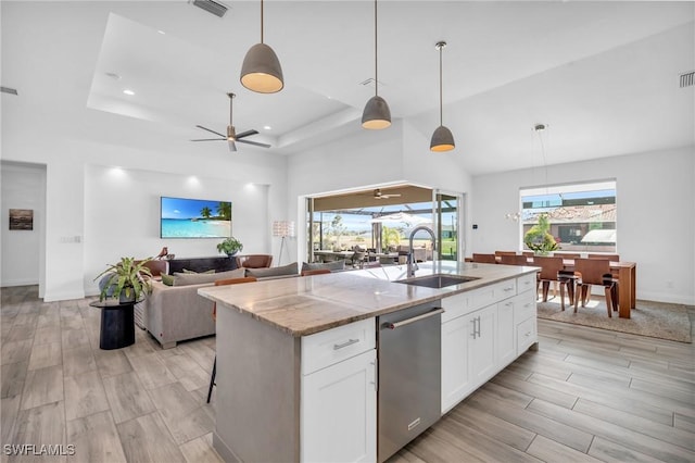 kitchen featuring sink, dishwasher, light stone countertops, white cabinets, and a center island with sink