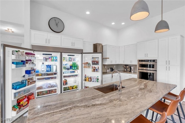 kitchen with pendant lighting, sink, white cabinetry, light stone countertops, and stainless steel double oven