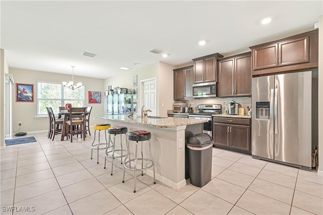 kitchen with a center island with sink, light tile patterned floors, a notable chandelier, and appliances with stainless steel finishes