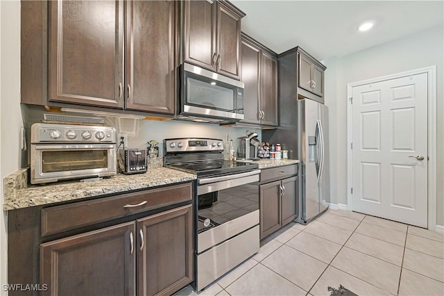 kitchen with stainless steel appliances, dark brown cabinets, light stone countertops, and light tile patterned floors