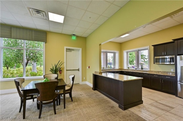 kitchen with stainless steel appliances, a drop ceiling, dark brown cabinets, and light stone counters