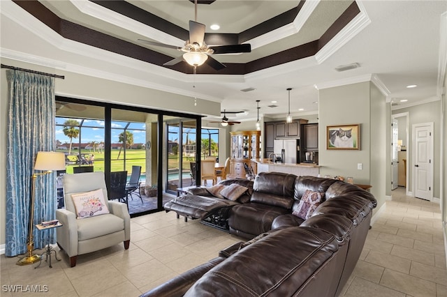 tiled living room with ceiling fan, a tray ceiling, and crown molding