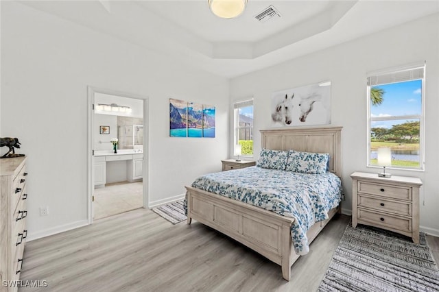 bedroom with light hardwood / wood-style floors, multiple windows, ensuite bathroom, and a raised ceiling