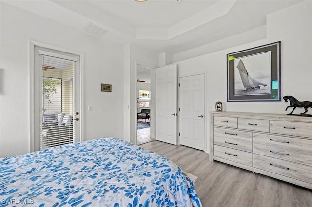 bedroom with light hardwood / wood-style flooring and a raised ceiling