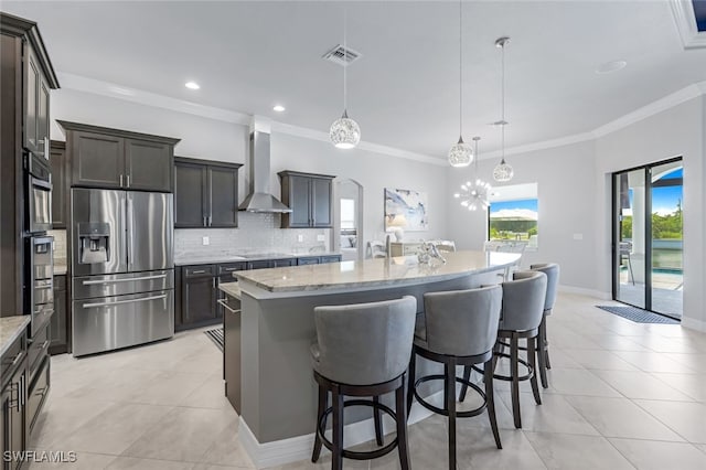 kitchen with decorative light fixtures, appliances with stainless steel finishes, wall chimney range hood, and a kitchen island with sink