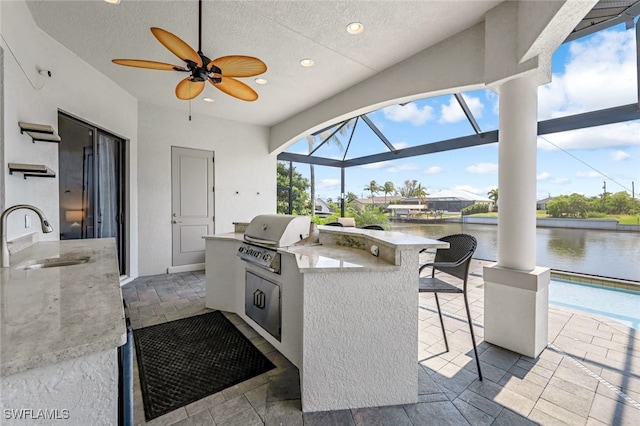 view of patio / terrace with a lanai, an outdoor kitchen, a grill, a wet bar, and a water view