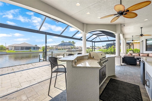 view of patio / terrace featuring a grill, a water view, a bar, ceiling fan, and exterior kitchen