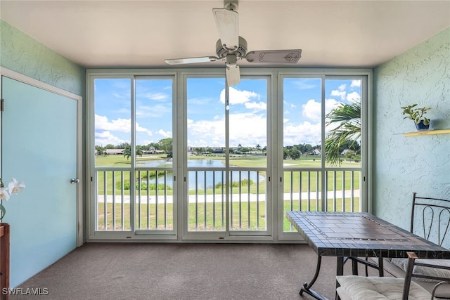 sunroom with ceiling fan and a water view