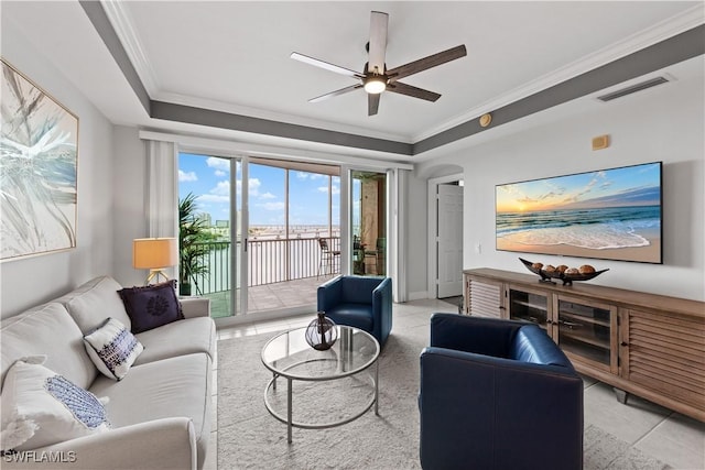 tiled living room with ceiling fan, a tray ceiling, and crown molding