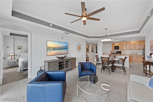 living room with ceiling fan, a raised ceiling, crown molding, and light tile patterned floors