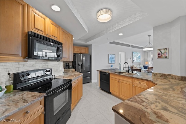 kitchen featuring light stone counters, black appliances, decorative backsplash, a tray ceiling, and sink