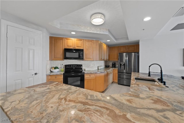 kitchen featuring light stone countertops, a raised ceiling, black appliances, light tile patterned floors, and sink