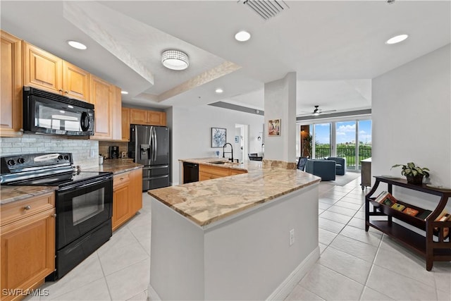 kitchen with a center island with sink, black appliances, light tile patterned floors, a tray ceiling, and sink