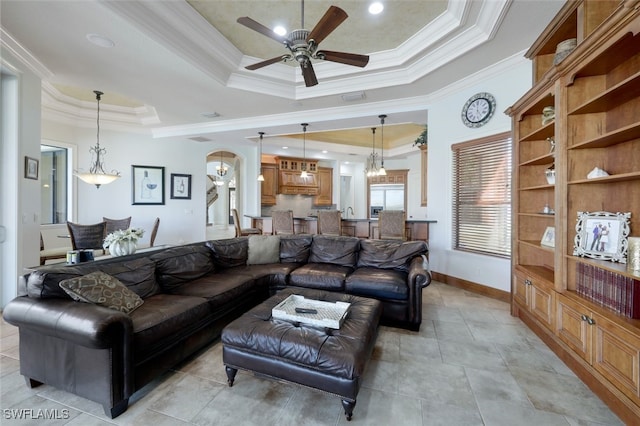 living room with ceiling fan, a tray ceiling, and crown molding