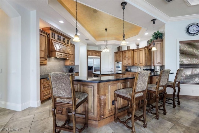 kitchen featuring appliances with stainless steel finishes, ornamental molding, pendant lighting, a kitchen bar, and a tray ceiling